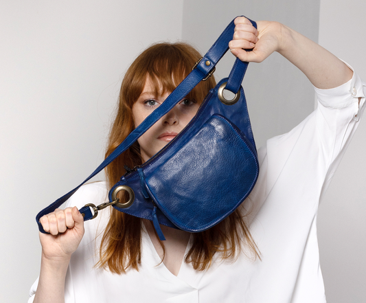 Person holding a blue leather bag against a plain background